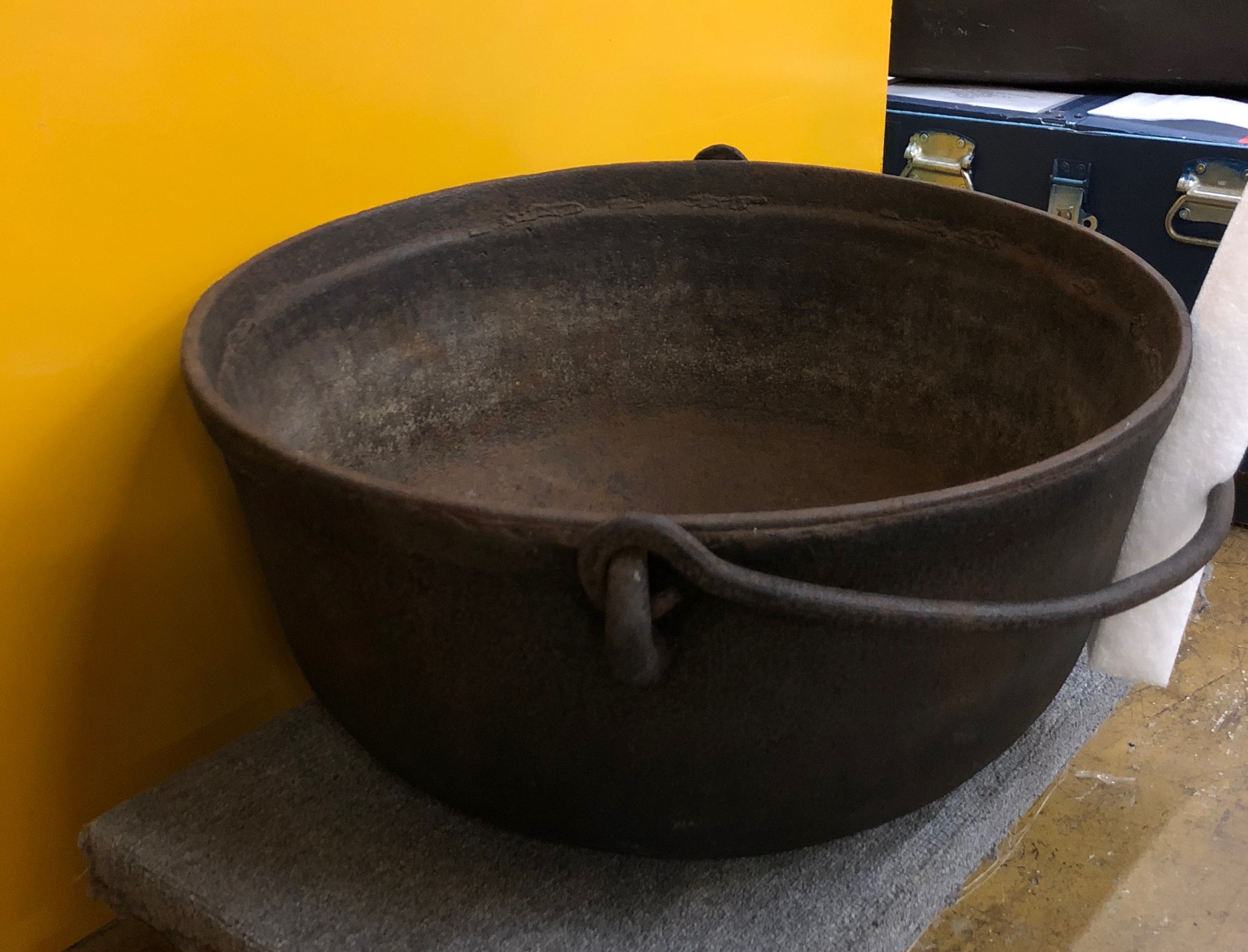 A colour photograph of an iron pot with handle, in artifact storage.